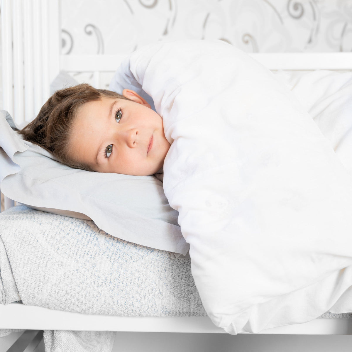 Child lying in a white bed under a duvet