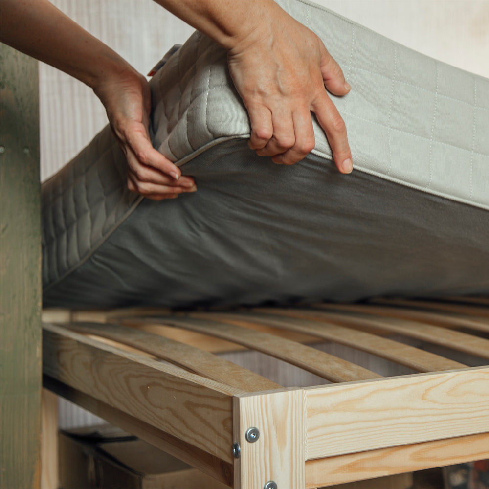 Hands lifting a mattress above a wooden slatted base