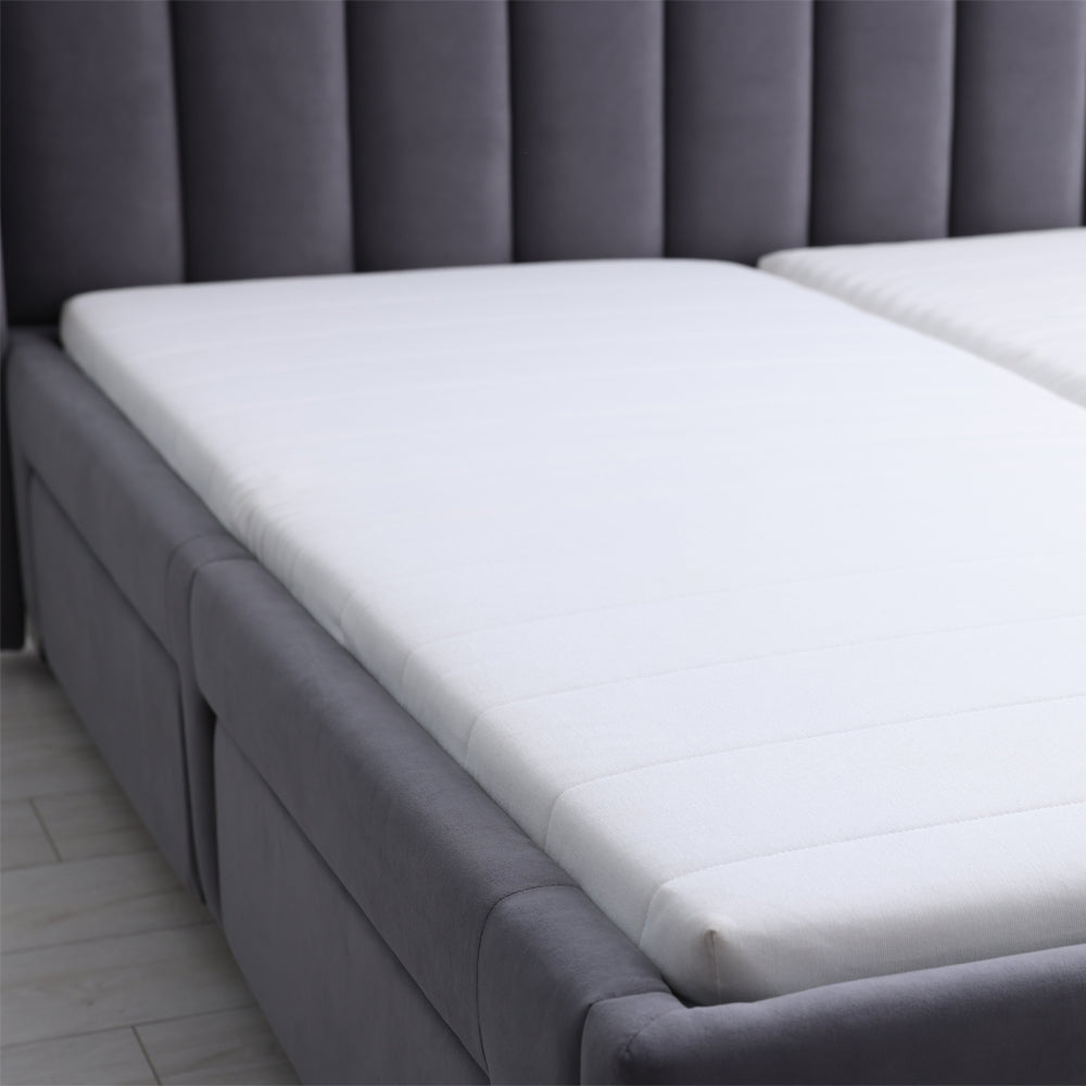 Two thin white toppers on an upholstered bed